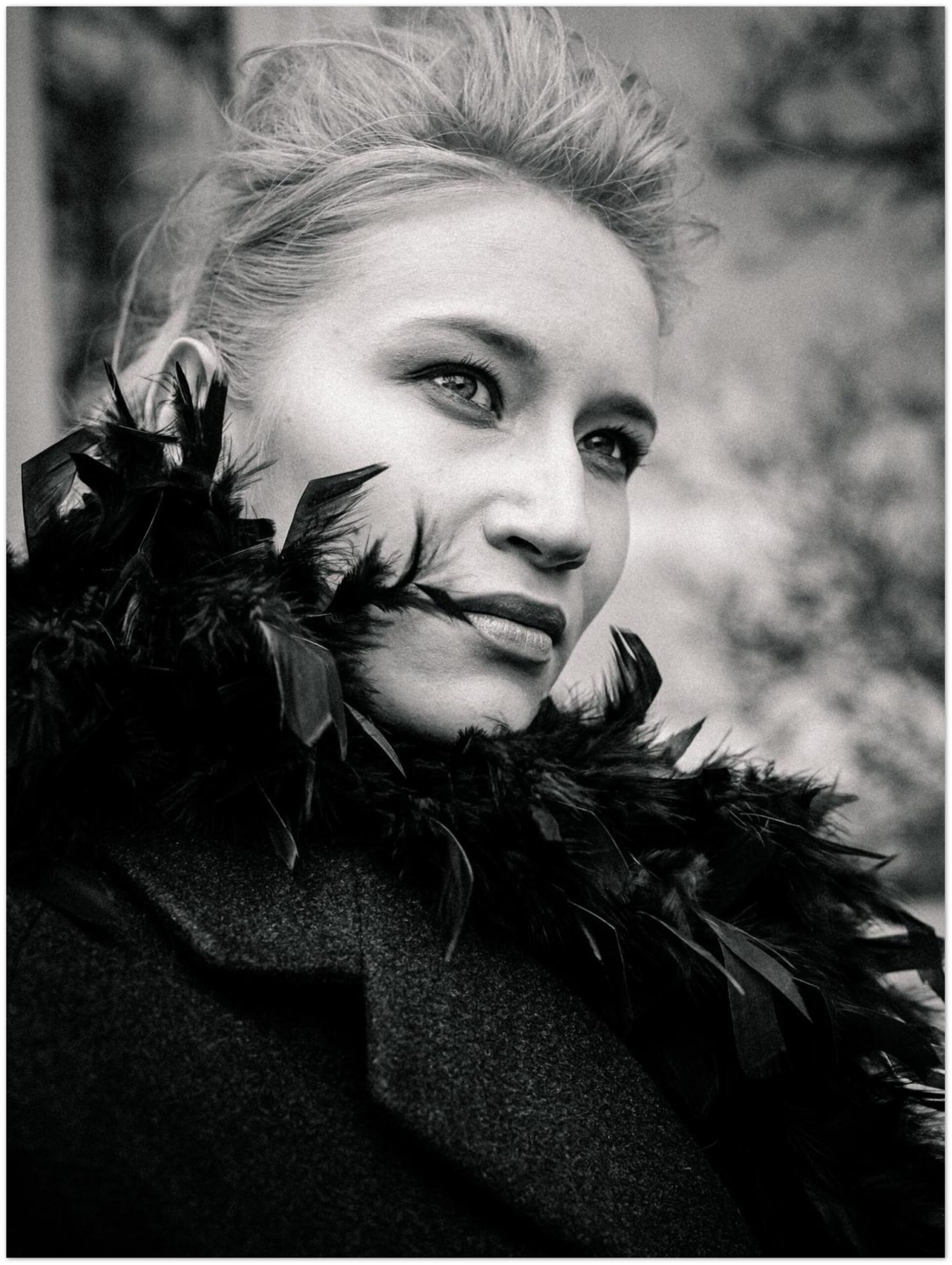 Outdoor Porträt einer Frau, die einen Wintermantel mit Federkragen trägt. Sie sieht seitlich am Betrachter vorbei, in die Ferne. Schwarzweiss Fotografie.